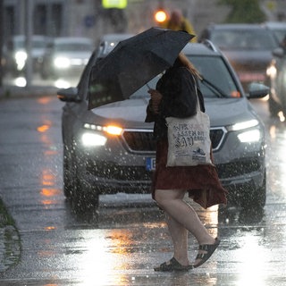 Eine Person in Regenmantel und mit Schirm überquert eine Straße in der Stadt bei Regen. So sah es am Montagabend vielerorts in Rheinland-Pfalz und weiten Teilen von Deutschland aus.