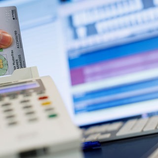 Eine Frau steckt eine Krankenkassenkarte in ein Lesegerät in einer Arztpraxis.