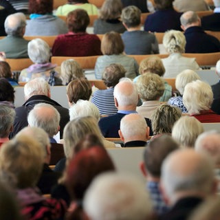 Zahlreiche Rentner sitzen auf Bänken 