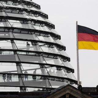 Neben der Reichstagskuppel in Berlin weht eine Flagge der Bundesrepublik Deutschland.