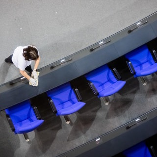 Eine Reinigungskraft putzt im Bundestag die Tischreihe vor der leeren Regierungsbank