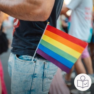 Ein Mann beim Christopher Street Day. Er hat in der Tasche seiner Hose eine kleine Regenbogen·fahne stecken. Rechts das SWR Logo für Leichte Sprache.