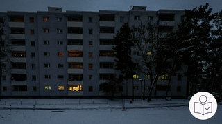 Ein Wohn·block im Dunkeln. In wenigen Fenstern brennt Licht. Vor dem Haus liegt Schnee. Daneben stehen große Bäume. Rechts das SWR Logo für Leichte Sprache.