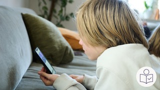 Ein Junge liegt auf einer Couch. Auf dem Bauch liegend schaut er auf ein Handy. Rechts das SWR Logo für Leichte Sprache.
