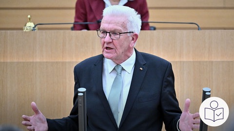 Der Minister·präsident Winfried Kretschmann hält seine letzte Rede. Er steht am Mikrofon im Landtag. Rechts das SWR Logo für Leichte Sprache.