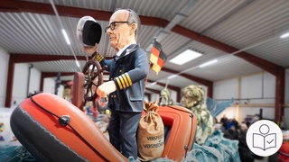 Eine Figur von Bundes·kanzler Merz als Kapitän in einem Schlauch·boot. Bundes·kanzler Merz hält das Steuer·ruder von dem Schlauch·boot. Rechts das SWR Logo für Leichte Sprache. 