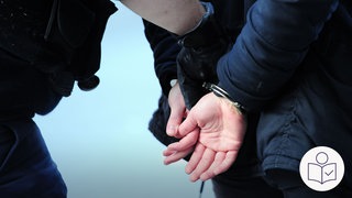 Eine Person hat Handschellen an. Die Hände sind hinter dem Rücken. Eine andere Person führt sie ab. Rechts das SWR Logo für Leichte Sprache.