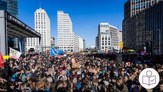 Viele Menschen auf einem Platz in Berlin. Hohe Häuser im Hintergrund. Viele Schüler demonstrieren gegen die Wehr·pflicht. Rechts das SWR Logo für Leichte Sprache.