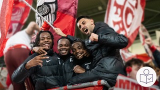 Fußball-Spieler vom SC Freiburg jubeln zusammen mit Fans. Im Hintergrund sind Fahnen. Der SC Freiburg hat ein Spiel in der Europa League gewonnen. Rechts das SWR Logo für Leichte Sprache.