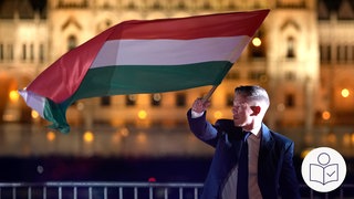Péter Magyar steht vor dem Parlament in Ungarn. Er schwingt eine Ungarn-Flagge. Péter Magyars Partei hat die Wahl in Ungarn gewonnen. Rechts das SWR Logo für Leichte Sprache.