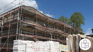 Ein Wohn·haus mit einem Gerüst. Das Haus hat drei Stockwerke. Vor dem Haus liegt Bau·material. Rechts das SWR Logo für Leichte Sprache. In Ingelheim gibt es bald 4 Hoffnungs·häuser.