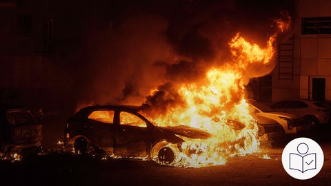 Es ist Nacht. Ein großes Feuer kommt aus einem Auto. In der Nacht hat Russland die Ukraine angegriffen. Darum haben Dinge gebrannt. Rechts das SWR Logo für Leichte Sprache.