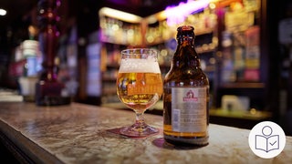 Ein Glas mit Bier steht auf der Theke von einer Kneipe. Daneben steht eine Bier·flasche. Rechts das SWR Logo für Leichte Sprache.