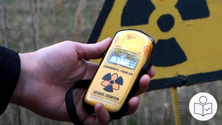 Eine Person hält ein Messgerät für radioaktive Strahlung. Dahinter ist das Symbol für Radioaktivität. Ein gelbes Dreieck mit schwarzen Zeichen. Rechts das SWR Logo für Leichte Sprache. 