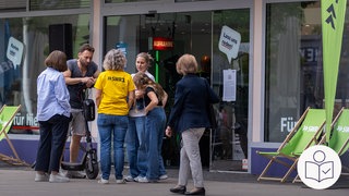 Menschen stehen vor dem Pop up-Studio von dem SWR in der Stadt Kaiserslautern. Rechts das SWR Logo für Leichte Sprache. 