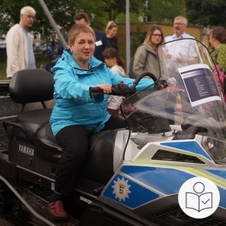 Eine Frau sitzt auf einem Schnee·mobil. Das Schnee·mobil ist von der Polizei. Die Polizei in Freiburg hat Menschen mit Behinderung zu einem Besuchs·tag eingeladen. Rechts das SWR Logo für Leichte Sprache.