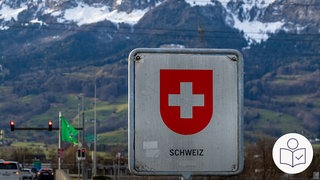 Ein Schild mit der Aufschrift Schweiz. Darüber ein weißes Kreuz auf einem roten Grund. Hinter dem Schild sieht man hohe Berge. Rechts das SWR Logo für Leichte Sprache. 
