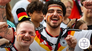 Zwei Männer im Deutschland-Trikot. Sie haben im Gesicht schwarz-rot-goldene Schminke. Sie schauen das Spiel von Deutschland gegen Curaçao bei der Fußball-WM. Rechts das SWR Logo für Leichte Sprache.