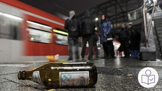 Auf dem Foto sieht man einen Bahn·hof. Im Vordergrund liegt eine Bier·flasche auf dem Boden. Rechts das SWR Logo für Leichte Sprache. 