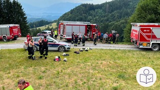 Auf dem Foto sieht man den Ort von dem Traktor·unfall. Viele Helfer sind dort. Man sieht auch Einsatz·fahrzeuge. Rechts das SWR Logo für Leichte Sprache. 