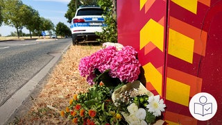 Blumen liegen an einer Straße. An der Stelle ist ein Student angegriffen worden. Der Student ist gestorben. Die Stelle ist in Trier an der Universität. Rechts das SWR Logo für Leichte Sprache.