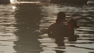 Zwei Frauen stehen in einem Badesee, eine trägt die andere durchs Wasser