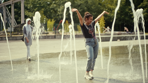 Zwei Teenagerinnen laufen durch einen Springbrunnen