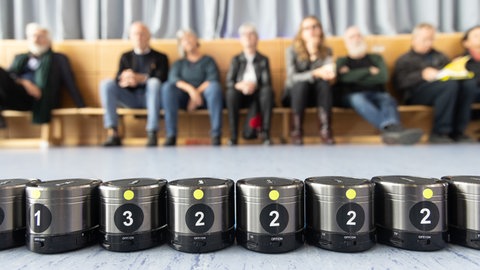 Reihe von Minilautsprechern, dahinter Reihe von sitzenden Menschen