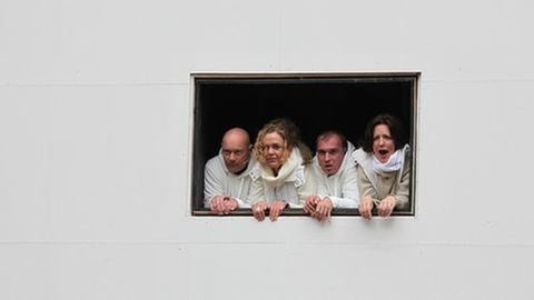Zwei Sängerinnen und zwei Sänger schauen auf einer fensterähnlichen Lucke