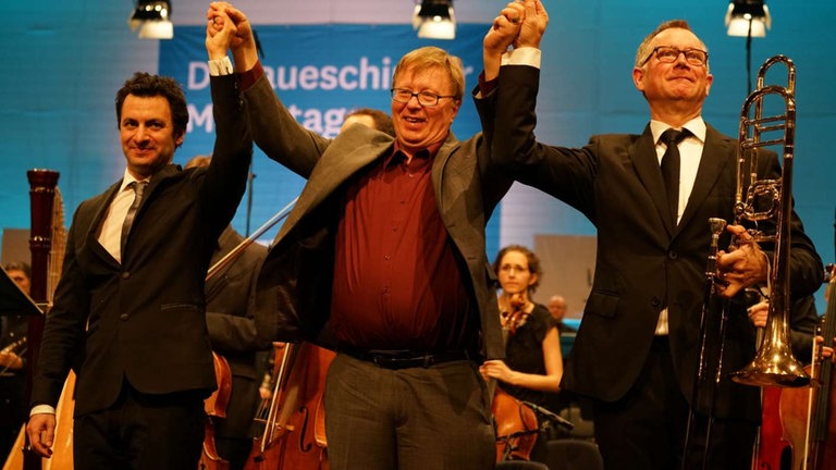 Drei Männer stehen auf de Bühne und bedanken sich