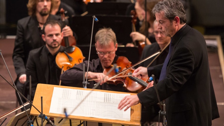 Mann, der dirigiert, schaut in die Partitur vor dem Orchester