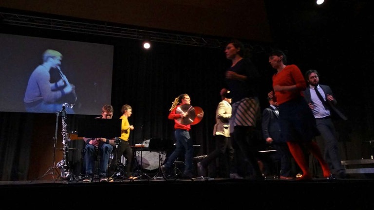 MusikerInnen des Nadar Ensembles laufen auf der Bühne herum