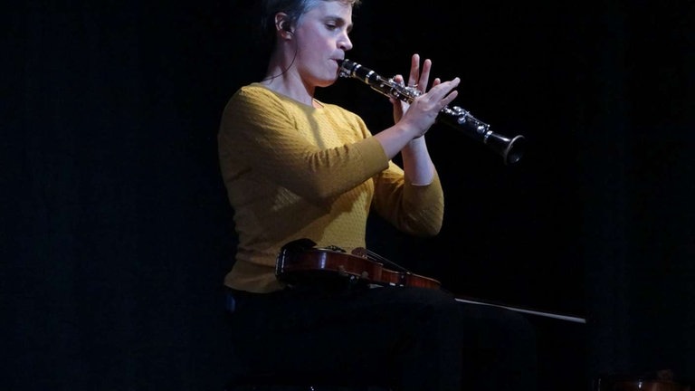 Frau spielt Klarinette mit Geige auf dem Schoß