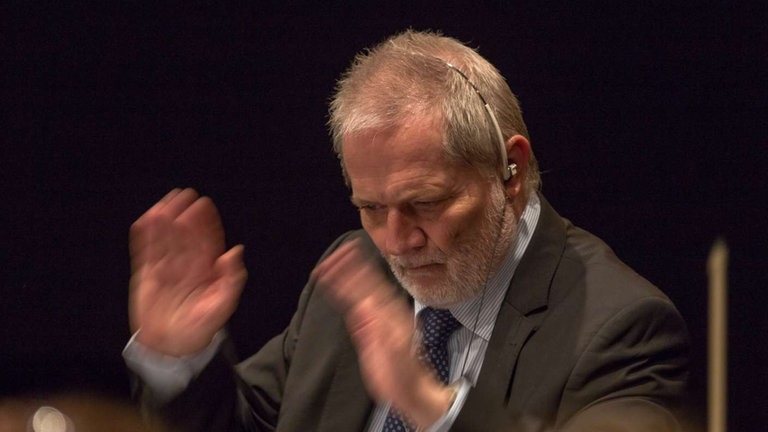 Mann mit bart und Headset dirigiert Orchester