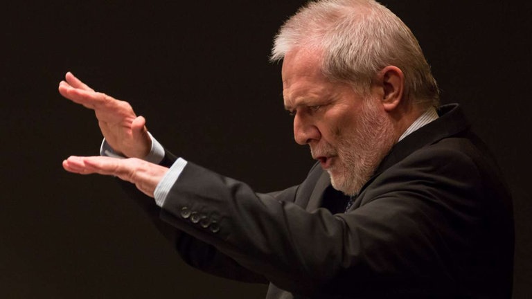 Mann mit Bart dirigiert Orchester