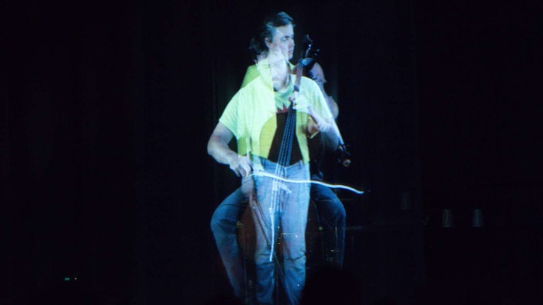 Foto von Videoleinwand. Zwei Musikerinnen, eine sitzen, eine stehend, sind "übereinander" gefilmt