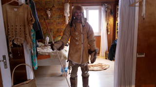 Mann steht in selbstgemachter Steinzeitkluft