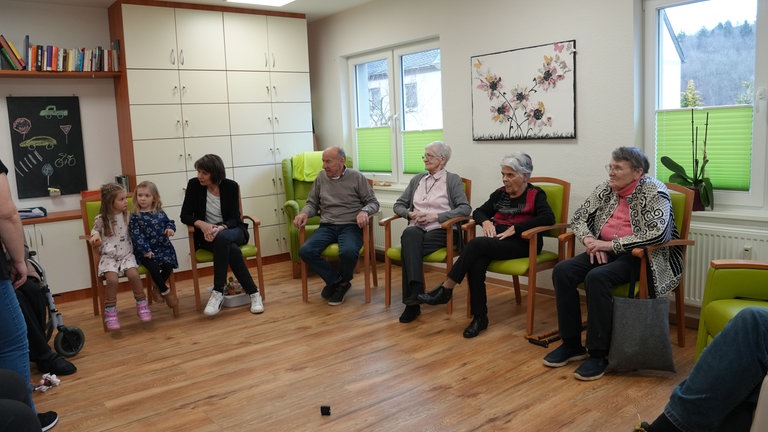 Eine Gruppe von jungen und alten Menschen sitzt in einem hellen Raum in einem Stuhlkreis.