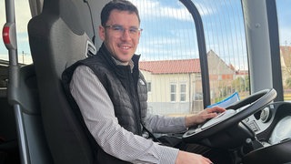 Ein Mann sitzt auf dem Fahrersitz eines Busses und lächelt in die Kamera