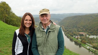 Junge braunhaarige Frau mit ihrem Vater. Die beiden tragen Kleidung zum Wandern. Im Hintergrund sieht man die Mosel und Weinberge.