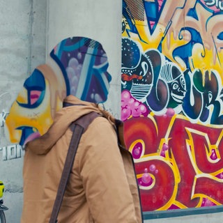 Frau läuft an einem Graffiti vorbei. Sie ist anonymisiert.