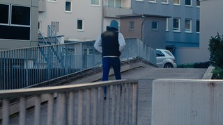 Ein großer muskulöser Mann läuft die Straße entlang. Er ist anonymisiert dargestellt, weil er eine lange Zeit im rechtsradikalen Milieu aktiv war.