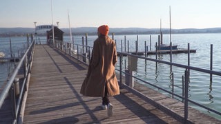 Junge Frau schlendert auf einem Steg am Bodensee