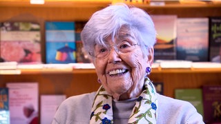 Buchhändlerin Brigitte sitzt in ihrem Buchladen in Konstanz. Sie sitzt vor einem Bücherregal und lächelt in die Kamera.