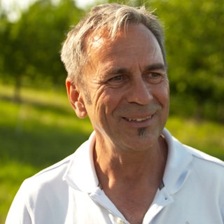 Ein Mann mittleren Alters steht in der Natur und lächelt 