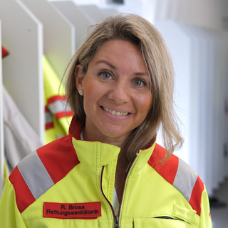 Ramona ist Quereinsteigerin im Rettungsdienst. Sie trägt ihre Einsatzbekleidung und lacht in die Kamera.