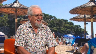 Harald, 73 Jahre alt, sitzt lächelnd als Gast in der Landesschau Baden-Württemberg. Er trägt ein buntes Hemd mit geometrischem Muster und eine Brille. Der Rentner aus Ravensburg erzählt von seiner zweiten Karriere als DJ.