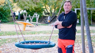 Spielplatzprüfer Michael steht vor einer Nestschaukel auf einem Spielplatz.