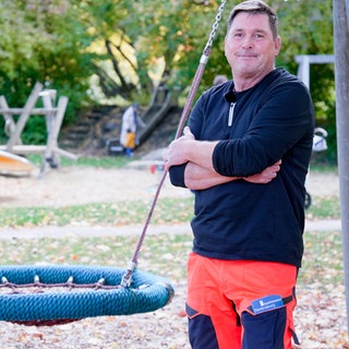 Spielplatzprüfer Michael steht vor einer Nestschaukel auf einem Spielplatz.