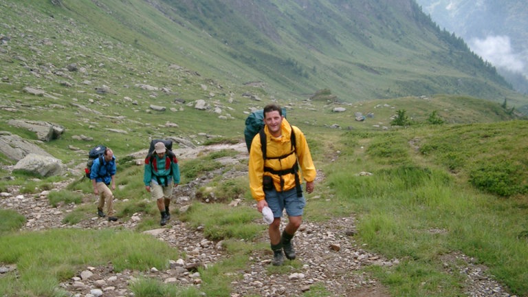 Fritz mit Freunden am Wandern in den Bergen auf einer großen Wiese.  